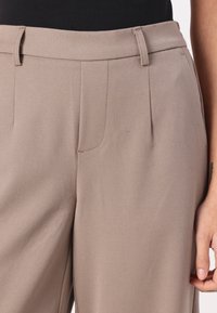 Beżowe spodnie o dopasowanym kroju z gładką teksturą, z płaskim przodem, dwiema kieszeniami oraz szlufkami na pasek w talii dla dodatkowego akcentu.
