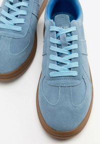 Wildledersneaker in Hellblau mit kontrastierenden blauen Schnürsenkeln. Abgerundete Zehenpartie, gepolsterter Schaft und braune Gummisohle. Schlichte, gestickte Details.