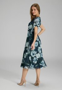 Robe fleurie dans des teintes de bleu marine et de vert, avec un corsage ajusté, des manches courtes bouffantes et une jupe fluide, fabriquée en tissu léger.