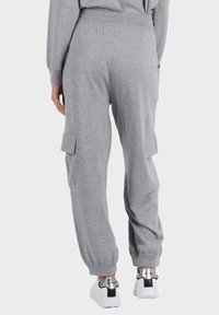 Pantaloni jogger grigi con vita elastica, tasche laterali a cargo e polsini a costine. Texture morbida e vestibilità ampia per il massimo comfort. Abbinati a sneaker bianche.