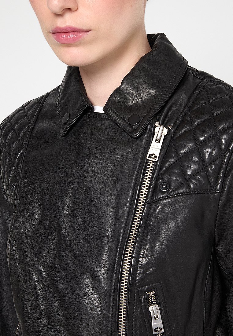 Giacca in pelle nera con design a spalle trapuntate, bottoni a pressione e zip silver. Texture morbida con silhouette aderente.