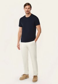 Marineblauwe short-sleeve t-shirt gecombineerd met crèmekleurige broeken en tan schoenen. Gladde stof, klassieke pasvorm en neutraal kleurenpalet.