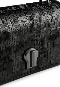 Schwarze Handtasche, bedeckt mit glänzenden Pailletten, mit einem glänzenden silbernen rechteckigen Verschluss auf weißem Hintergrund.