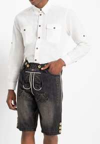 Camicia bianca di lino con bottoni marroni, due tasche sul petto. Pantaloni corti in denim scuro con intricate ricami dorati e dettagli con bottoni ai lati.