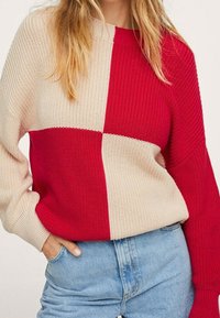Sweter z dzianiny o designie w blokach kolorystycznych w kolorze czerwonym i kremowym. Charakteryzuje się luźnym krojem, szerokimi rękawami i prążkowaną teksturą.
