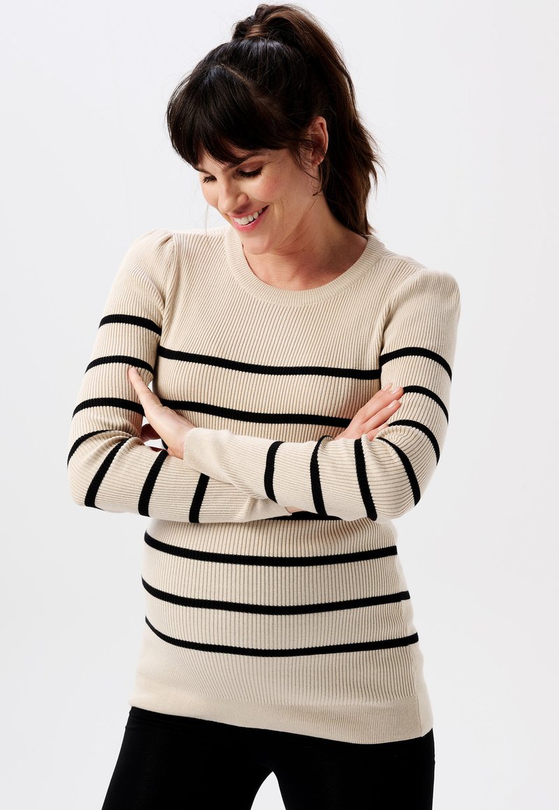 Beige Rippstrickpullover mit horizontalen schwarzen Streifen, rundem Ausschnitt und leicht gepufften Schulterdetails, kombiniert mit schwarzen Hosen.