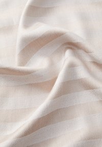 Tissu léger arborant des rayures alternées crème et beige doux. Le tissage texturé crée un motif subtil à la surface.