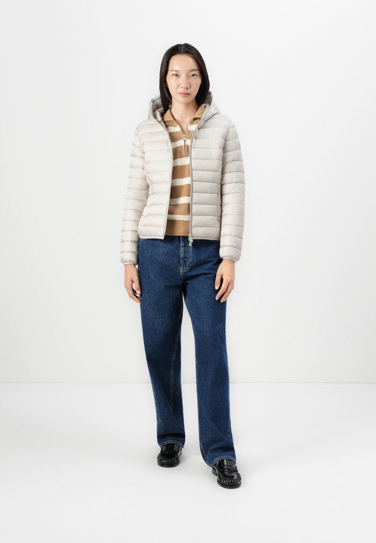 Doudoune gris clair avec un matelassage horizontal, fermeture éclair à l'avant et capuche, associée à un pull rayé marron et un pantalon en jean bleu à jambes larges.