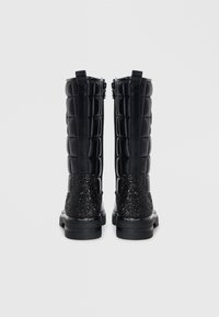 Black knee-high boots feature a quilted synthetic upper, glittery black heel accents, and a flat sole with a side zipper for easy wear.