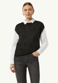 Czarny dzianinowy kamizelka z teksturowanym wzorem, noszona na białej koszuli z kołnierzykiem, w połączeniu z ciemnymi dżinsami.