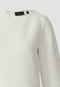 Weißes, strukturiertes Langarmshirt mit rundem Ausschnitt. Es verfügt über ein erhabenes Rautenmuster und einen kleinen Reißverschluss auf der Rückseite.