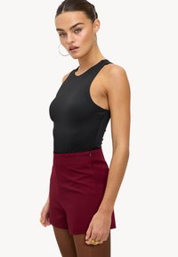 Body noir sans manches associé à un short taille haute bordeaux, avec une texture lisse, un design minimaliste et une fermeture éclair latérale.