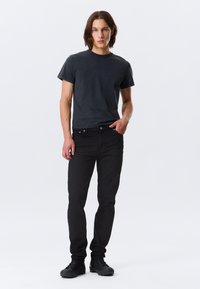 Black cotton t-shirt with short sleeves, paired with slim-fit black jeans. The outfit is complemented by black shoes. Minimalist design.