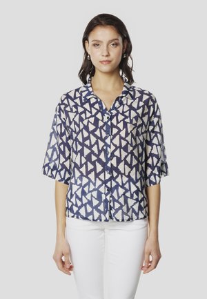 Camisa de manga corta con botones en azul marino con un patrón abstracto de triángulos blancos, tela ligera, ajuste relajado y cuello con solapa.