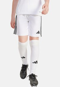 Weiße Fußballshorts mit schwarzen Seitenstreifen und passendem schwarzen Adidas-Logo. Weiße Kniestrümpfe mit schwarzen Akzenten. Schwarze Fußballschuhe.