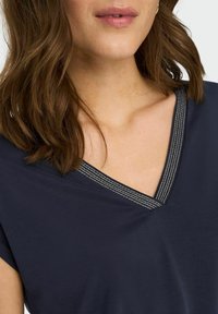 Haut en v à col marin avec manches courtes, présentant un accent texturé argenté autour de l'encolure. Tissu doux et coupe décontractée.