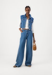 Denim jakna s ovratnikom in gumbnim zapiranjem, kombinirana s širokimi modrimi hlačami. Dodatki vključujejo rjavo torbico in čevlje z živalskim vzorcem.