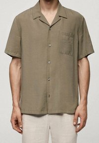 Kortärmlig knappljus olivgrön skjorta i lätt tyg, med en bröstficka, subtil textur och metallknappar.