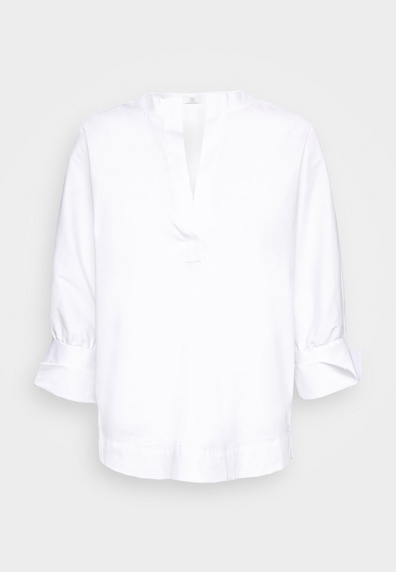Blouse blanche à manches longues avec encolure en V fendue et poignets retroussés, présentée sur un fond clair uni.