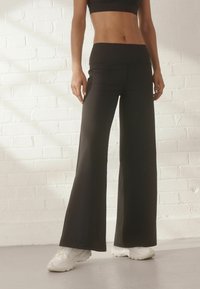 Black wide-leg pants with a high waistband, featuring a smooth texture and fitted silhouette, paired with white athletic shoes.