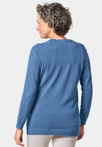 Pull en tricot bleu avec des manches longues, des bords côtelés et un design à ourlet haut-bas. Texture douce et col rond classique.