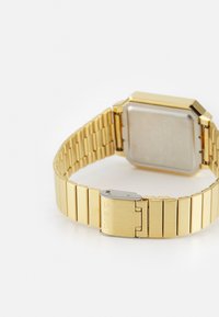 Reloj de metal dorado con una caja rectangular, una esfera plana y un diseño de pulsera de eslabones. Presenta un cierre plateado con "CASIO" grabado.