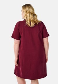 Korte wijnrode jurk met korte mouwen, relaxte pasvorm, katoenen materiaal, gladde textuur, knielange zoom, eenvoudig ontwerp zonder patronen of versieringen.