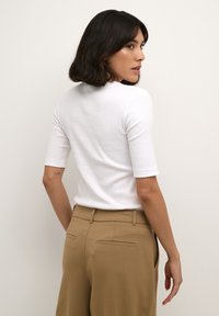 White short-sleeve t-shirt with a round neck, paired with light brown high-waisted trousers featuring back jet pockets. Smooth cotton texture.