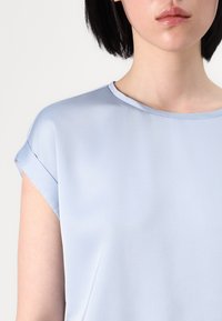 Top azzurro chiaro a maniche corte con una texture liscia e scollatura rotonda, con maniche arrotolate e una vestibilità comoda.
