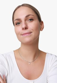 Silberne Kettenhalskette mit einem ovalen Perlenanhänger, der ein feines, zartes Design aufweist. Getragen von einem Modell mit einem gerippten weißen Top.
