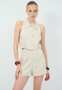 Beige gestreept twee-delig outfit met een mouwloze top met een brede kraag en knopen, gecombineerd met high-waisted shorts. Glad textuur.