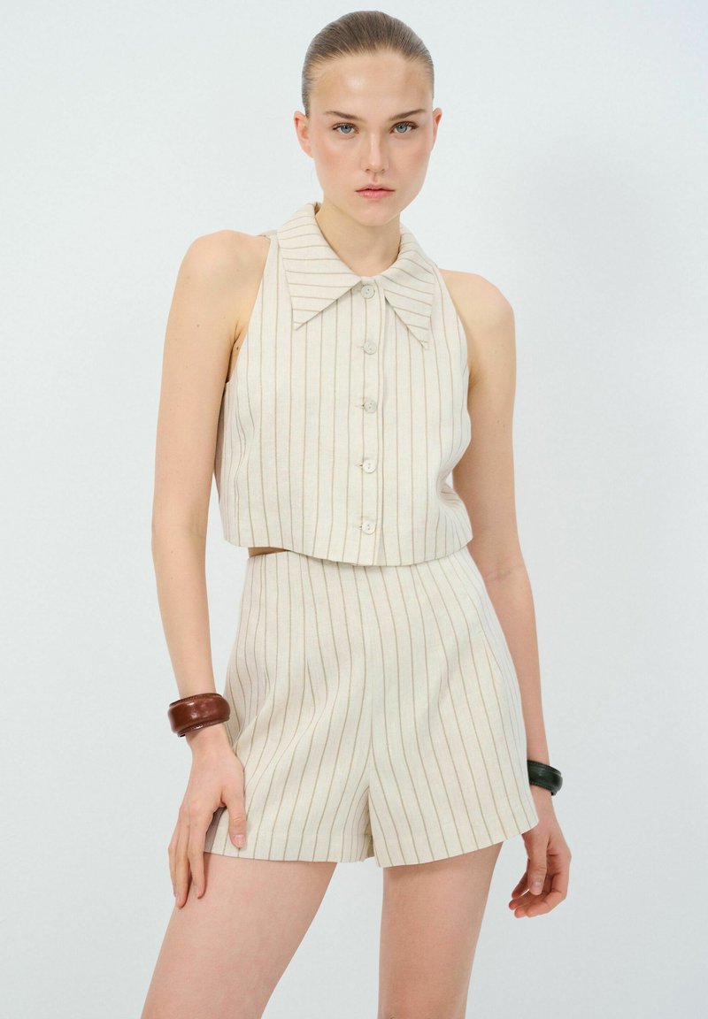 Beige gestreept twee-delig outfit met een mouwloze top met een brede kraag en knopen, gecombineerd met high-waisted shorts. Glad textuur.