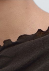Dark brown fabric with a soft texture, featuring a scalloped neckline. Close-up view highlights the material and detail of the edges.