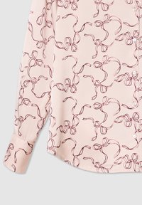 Blusa rosa chiaro con un motivo a fiocco ripetuto in rosso scuro, realizzata in tessuto morbido, con chiusura a bottone e maniche lunghe con polsini.