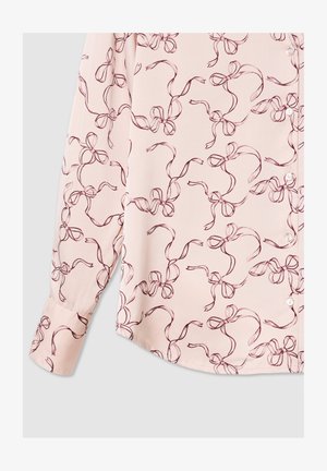 Blusa rosa chiaro con un motivo a fiocco ripetuto in rosso scuro, realizzata in tessuto morbido, con chiusura a bottone e maniche lunghe con polsini.