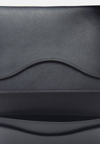 Sac à main en cuir noir avec une surface texturée, un accent incurvé sur le rabat et un design élégant et minimaliste. Intérieur doublé, sans quincaillerie visible.