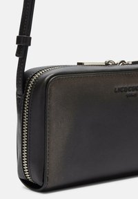 Czarna skórzana torba na ramię o gładkiej fakturze, z zamknięciem na zamek błyskawiczny, srebrnymi akcentami i tłoczonym logo z przodu.