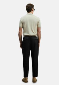 Lichtbeige polo met korte mouwen gecombineerd met zwarte tapered broeken. De broeken hebben twee achterzakken en zijn gemaakt van een gestructureerde stof.