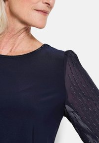 Navy-Kleid mit rundem Ausschnitt und glitzerndem Besatz, durchsichtigen Tüll-Puffärmeln, die mit vertikalen Strassakzenten verziert sind.