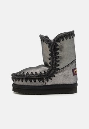 Metalická strieborná členková čižma s jemnou textúrou, dekoratívnym šitím v tmavošedej farbe, textúrovanou podrážkou a malou značkovou etiketou na boku.