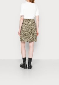 Top corto bianco a maniche corte abbinato a una gonna a campana verde oliva con fantasia a pois neri e bianchi. Stivali neri alla caviglia completano il look.