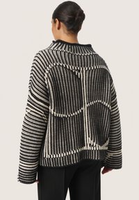 Strickpullover mit schwarz-weißem Streifenmuster, übergroßer Silhouette und strukturierten Details entlang der Nähte und Schultern.