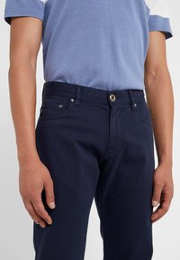 Námořnické modré bavlněné kalhoty s texturovaným povrchem, předními kapsami a kovovým zapínáním na knoflík. Nosit s světle modrou košilí.