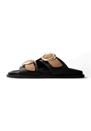 Czarna klapka na płaskiej podeszwie z dwoma szerokimi paskami, z których każdy ma dużą złotą klamrę i jasnobrązowe teksturowane dodatki, na białym tle.