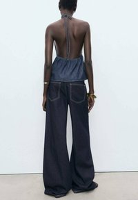 Denim-Haltertop mit offenem Rücken, kombiniert mit hoch taillierten, weit geschnittenen dunklen Jeans. Verfügt über helle Nähte und Gesäßtaschen.