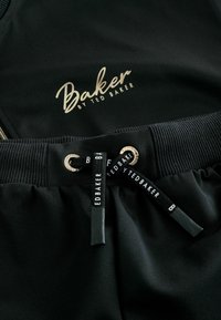 Čierne športové oblečenie s logom "Baker by Ted Baker" v zlatej farbe. Pás so sťahovacou šnúrkou a čiernymi logovanými šnúrkami, s rebrovanou textúrou.