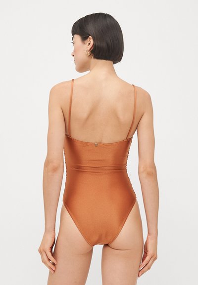 Back view of a rust-colored one-piece swimsuit with thin straps, a low back, and a fitted design. Smooth texture and minimal hardware detail.