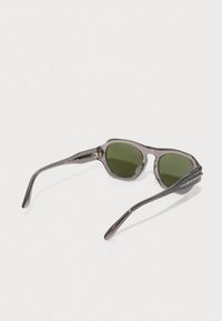 Oglinzi de soare gri transparente cu lentile verzi, rame rotunde și accente metalice elegante pe temples, având un design minimalist.