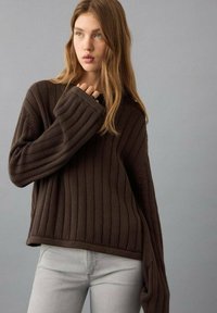 Brauner, gerippter Strickpullover mit weiten Ärmeln, lockerem Schnitt und strukturiertem Muster. Kombiniert mit hellgrauen, eng anliegenden Jeans. Schlichtes, modernes Design.