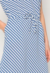 Robe en coton présentant un motif à rayures diagonales bleu et blanc, avec une taille à cordon et des poches latérales. Texture lisse.